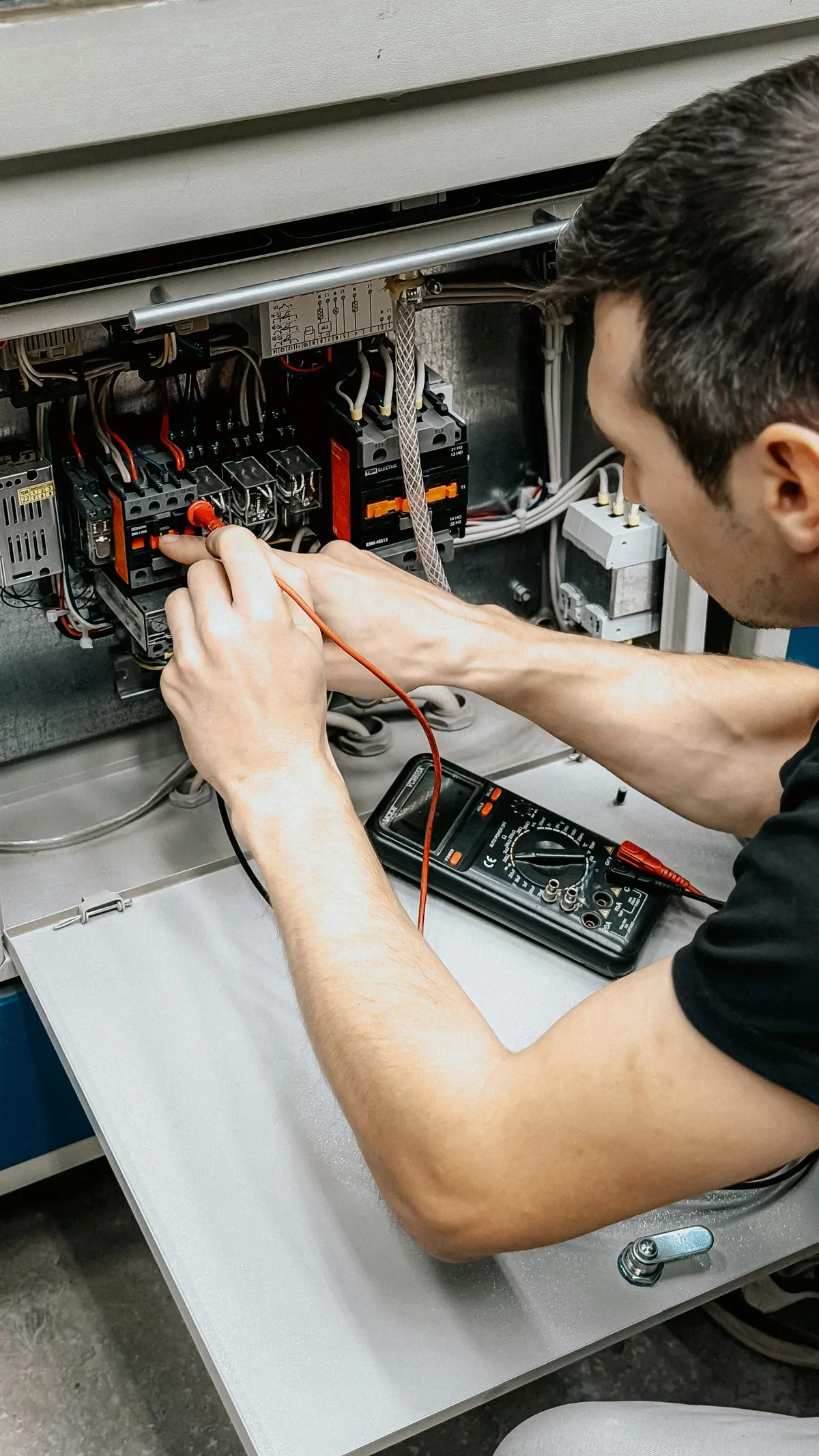 Electrician using a multimeter to check voltages on a control panel